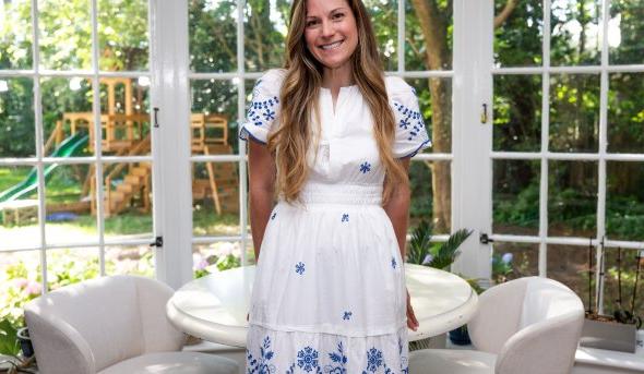 A woman in a white dress leans in a table in a room 